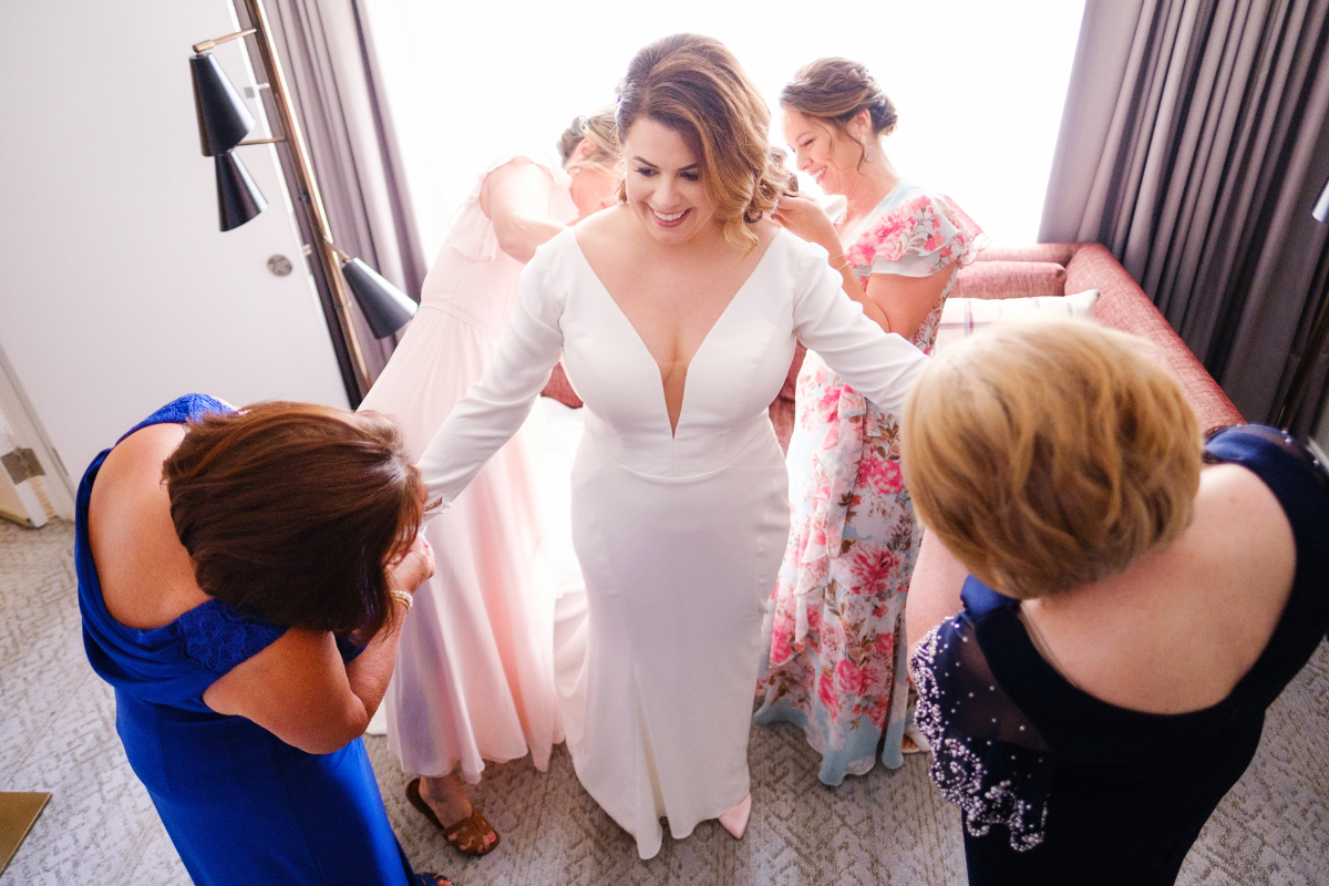 brides entourage helps her get into her wedding dress