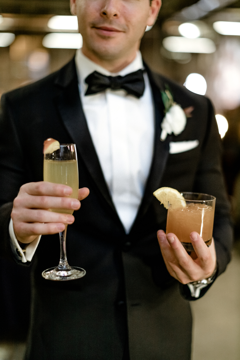 groom holds two signature cocktails