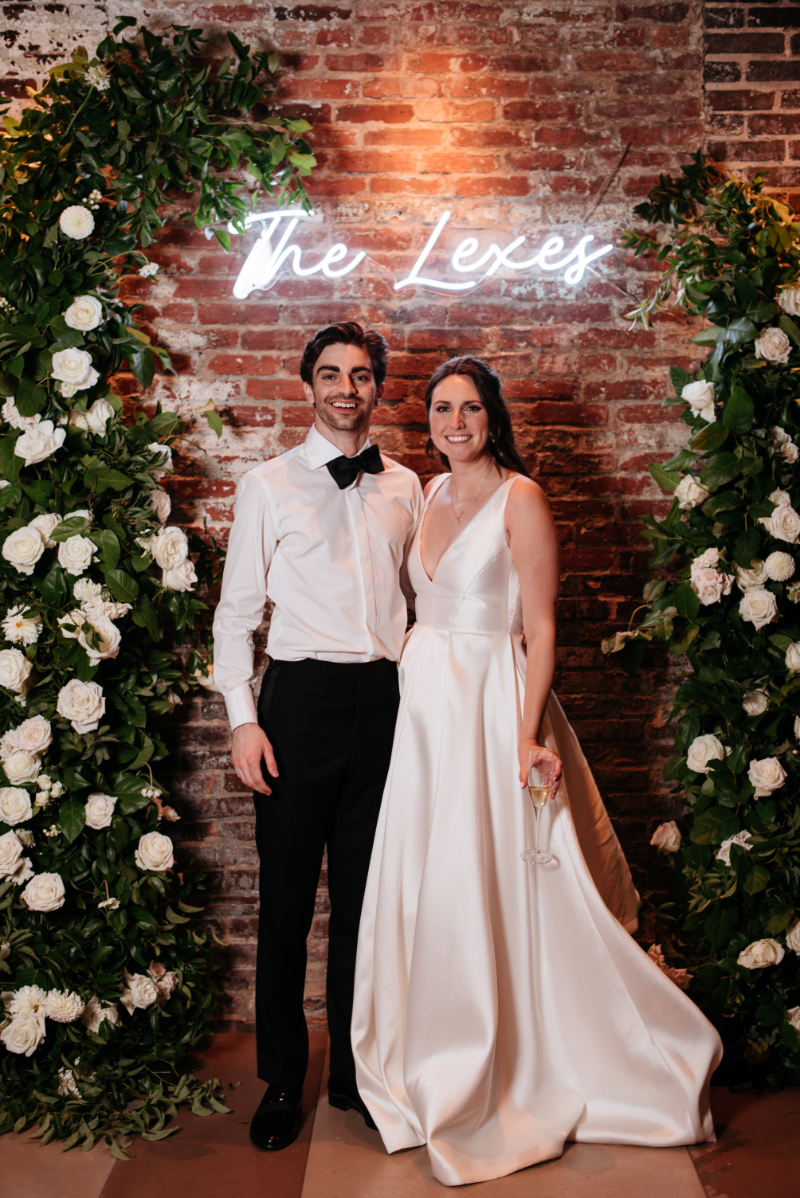 bride and groom stand underneath neon sign