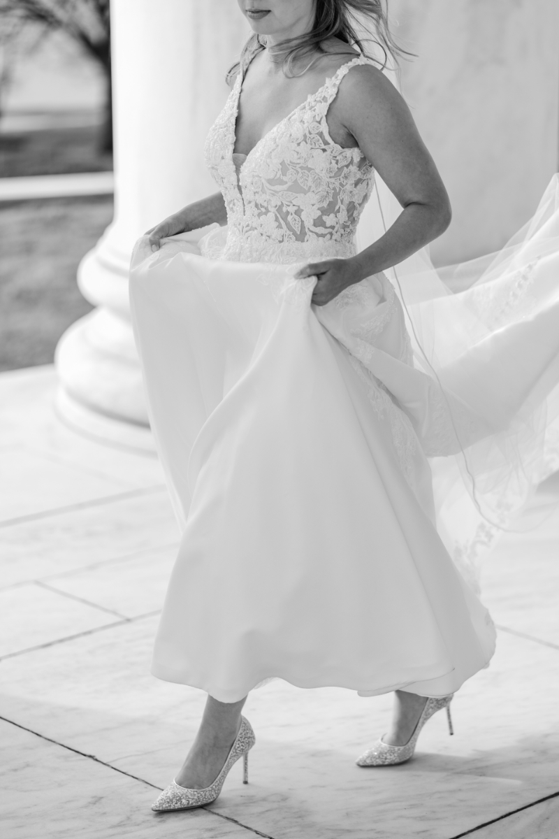 BLACK AND WHITE OF BRIDE HOLDING UP HER DRESS WITH A PEEK OF HER BRIDAL SHOES